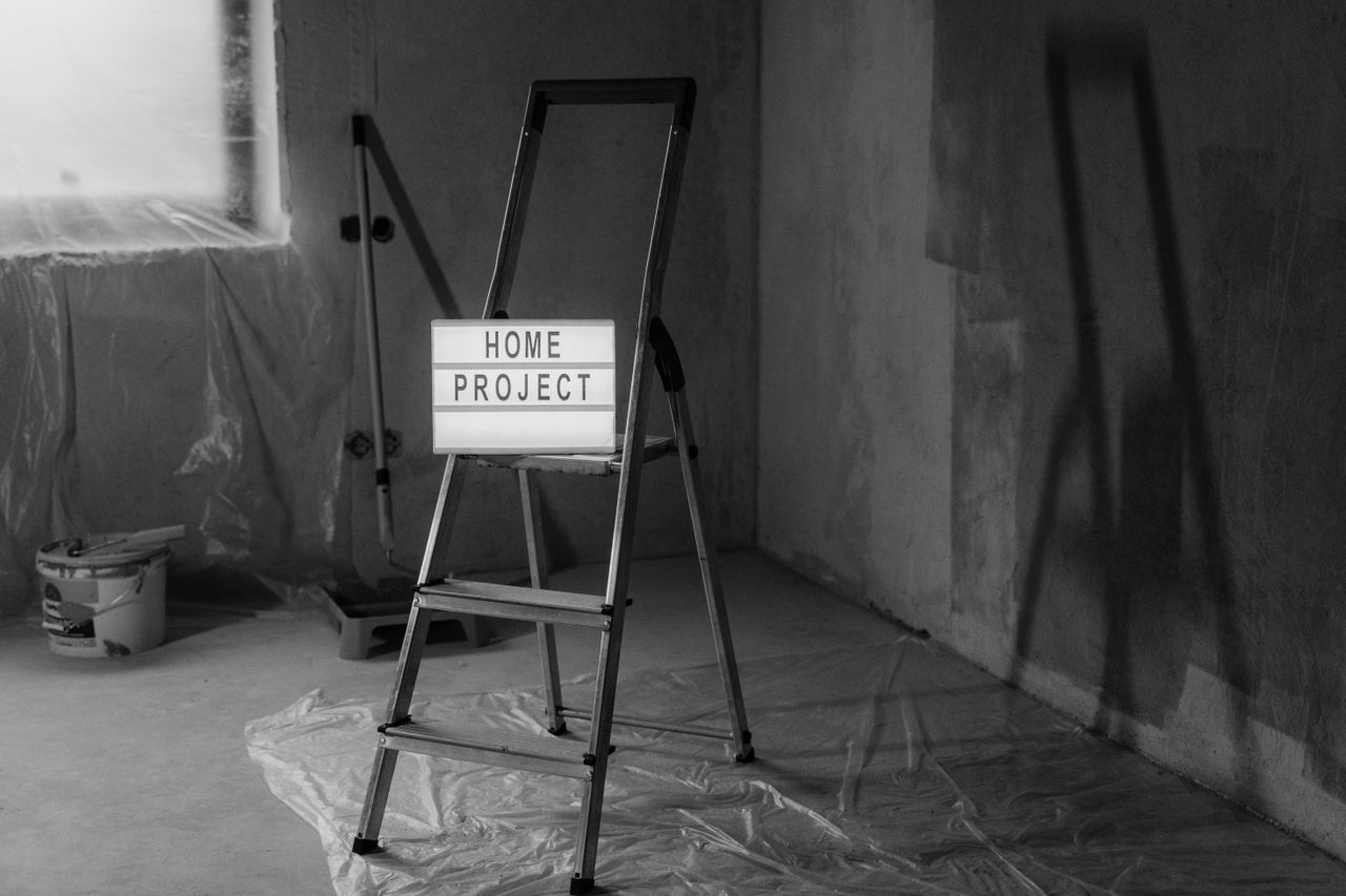 Black and white image of a step ladder with a home project sign in a renovation setting.